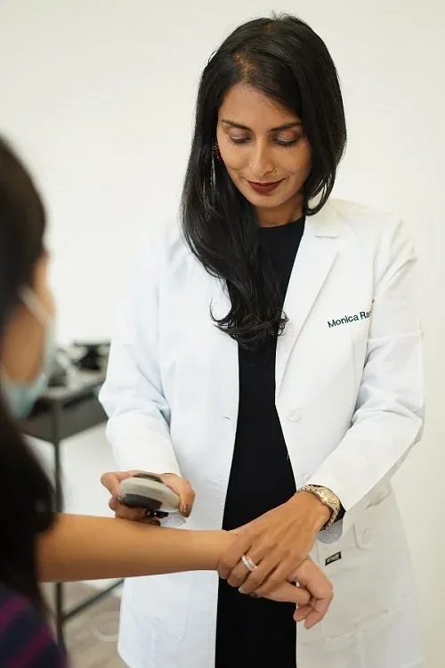 Dr. Monica Rani checking a masked patient's forearm with a handheld dermatoscope