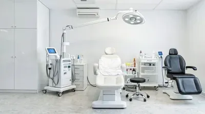 Bright treatment room with two procedure chairs, an overhead exam light and a device cart
